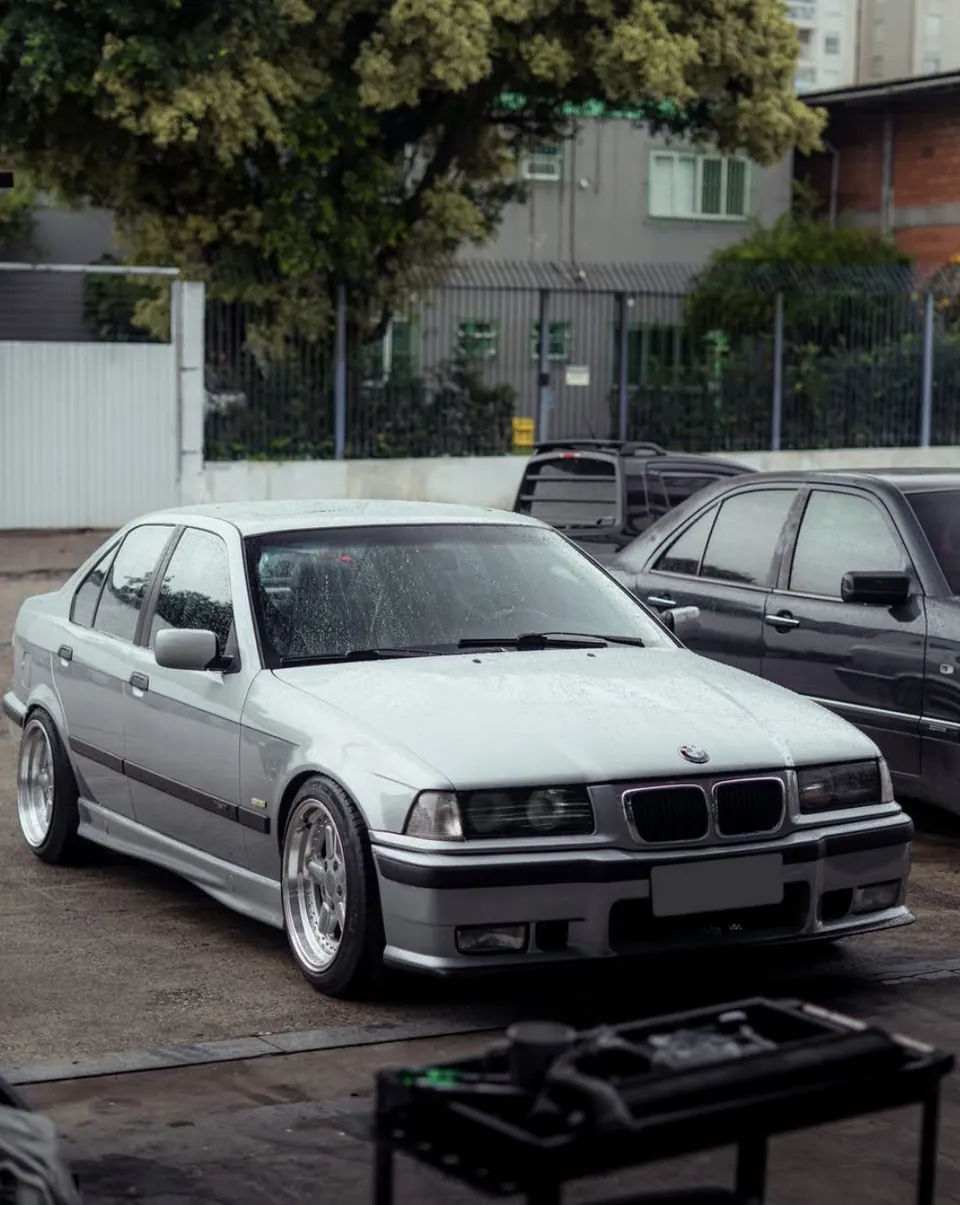 E36 sedã prata com rodas polidas no pátio da oficina depois da chuva